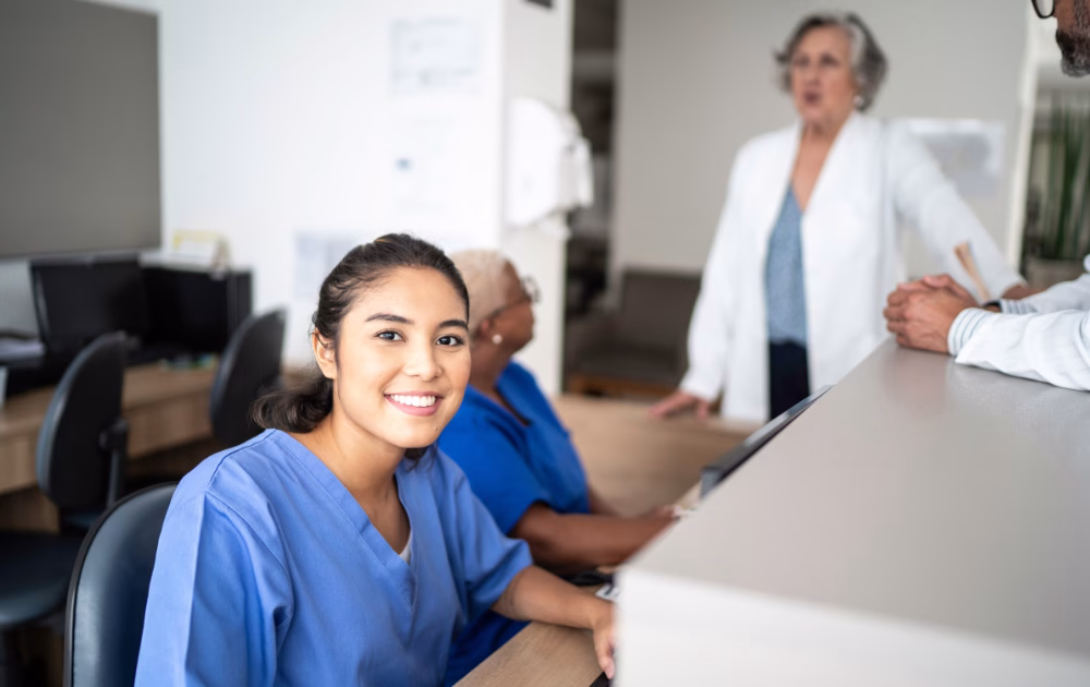 a nurse smiling in a hospital reception along with another nurse and doctors