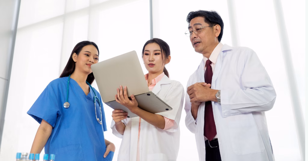 an asian doctor, his clinic manager, and nurse having a conversation with laptop in the clinic lobby