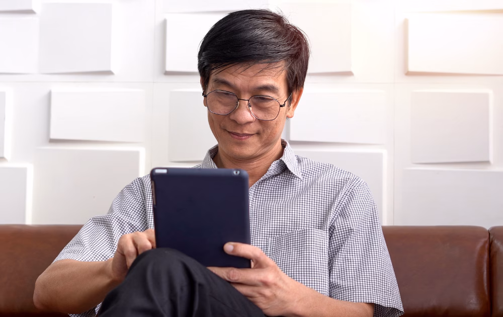 an asian man reading an article in a tablet sitting down in the living room